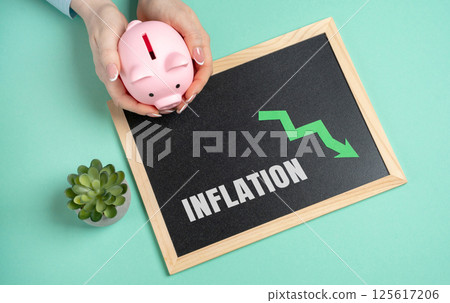 Inflation concept. Rate at which the general level of prices for goods and services rises, reducing the purchasing power of money over time. Piggy bank in woman's hands and board with inscription 125617206