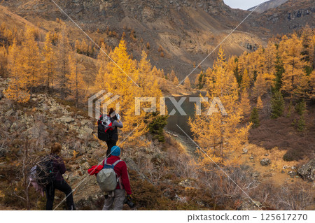 Hikers exploring mountain landscape with autumn trees near a serene lake 125617270
