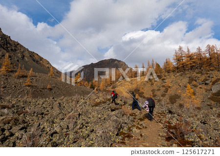 Hikers exploring autumn mountain trail surrounded by sparse trees and rocky terrain 125617271
