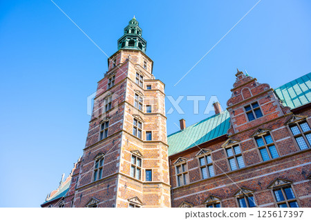 The Rosenborg Castle Tower stands tall in Copenhagen, showcasing its intricate architecture against a bright blue sky. Visitors admire its unique design and historical significance. The Rosenborg Castle Tower stands tall in Copenhagen, showcasing its intricate architecture against a bright blue sky. Visitors admire its unique design and historical significance. 125617397