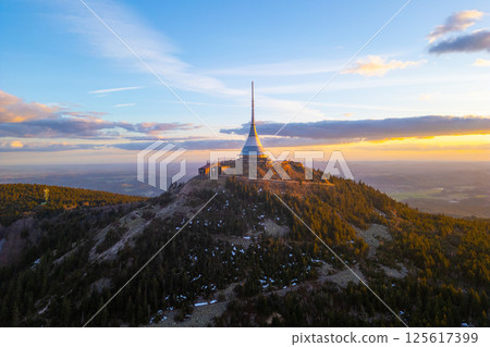Spring colors illuminate Jested Mountain as the sun sets over Liberec. The iconic tower stands tall, surrounded by nature's beauty and a serene atmosphere at dusk. 125617399