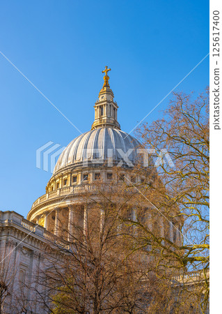 St. Paul's Cathedral stands majestically against a clear blue sky, showcasing its iconic dome. The surrounding trees add a touch of nature to this historic London landmark. 125617400