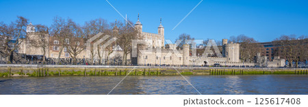 Visitors admire the historic Tower of London from Tower Wharf, enjoying the clear blue sky and the reflections on the River Thames. The tower stands as a symbol of history and strength. 125617408