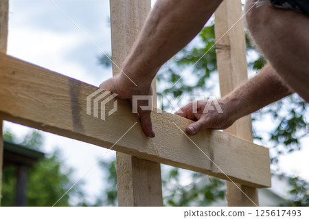 Close-up of man's hands precisely leveling wooden board for construction project. Image captures moment of concentrated woodworking Close-up of man's hands precisely leveling wooden board for construction project. Image captures moment of concentrated woodworking 125617493