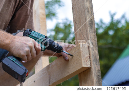 Hands of man using drill to assemble wooden structure. Precision and skill required in DIY construction 125617495