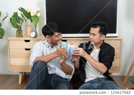 Friendship and Coffee Moments. Two men toasting with coffee mugs in a relaxed living room. Friendship and Coffee Moments. Two men toasting with coffee mugs in a relaxed living room. 125617982