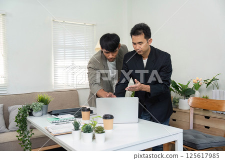 Team Collaboration and Project Review. Two professionals working together on a laptop in a modern office setting. Team Collaboration and Project Review. Two professionals working together on a laptop in a modern office setting. 125617985