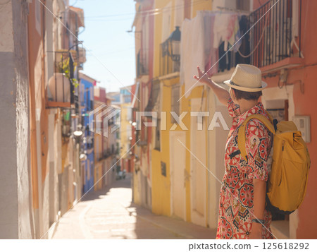 Woman in dress strolls through colorful streets of Spanish coastal town of La Vila Joiosa or Villajoyosa. sunny winter atmosphere highlights charm of Mediterranean architecture and quiet seaside life 125618292