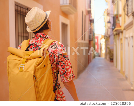 Woman in dress strolls through colorful streets of Spanish coastal town of La Vila Joiosa . sunny winter atmosphere highlights charm of Mediterranean architecture and quiet seaside life, back view Woman in dress strolls through colorful streets of Spanish coastal town of La Vila Joiosa . sunny winter atmosphere highlights charm of Mediterranean architecture and quiet seaside life, back view 125618296