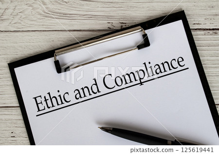 Clipboard with a document titled Ethic and Compliance text, placed on a white wooden surface. 125619441