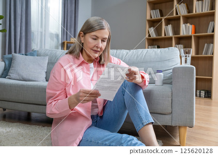 Mid aged woman in pink shirt reading description to medicine and looking concentrated 125620128