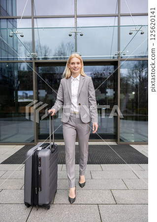 Confident businesswoman walking with suitcase during departure for corporate trip in city Confident businesswoman walking with suitcase during departure for corporate trip in city 125620141