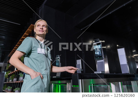 Blonde young doctor holding access card in her hand and looking aside Blonde young doctor holding access card in her hand and looking aside 125620160