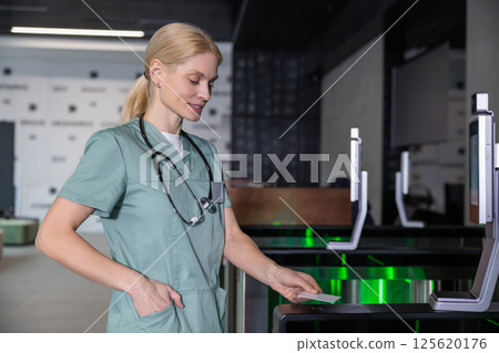 Female doctor in lab coat passing through security control by using access card 125620176