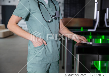 Female doctor in lab coat passing through security control by using access card 125620178