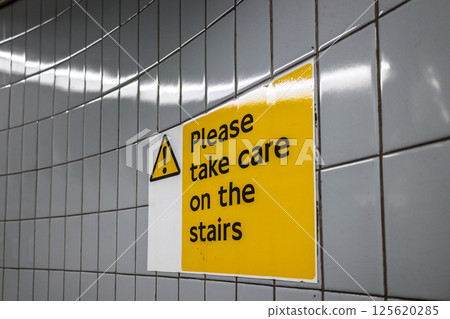 Caution sign on tiled wall warning pedestrians to take care on the stairs indoors 125620285