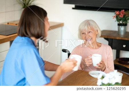 Medical caregiver drinking tea with senior patient offering assistance and care Medical caregiver drinking tea with senior patient offering assistance and care 125620295