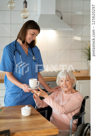 Young caregiver giving tea to senior woman in room Young caregiver giving tea to senior woman in room 125620297