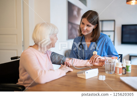 Female doctor providing assistance to senior patient taking test for blood pressure measurement 125620305
