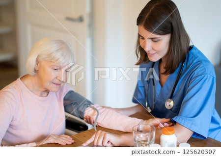 Medical professional helping elderly patient with blood pressure and pulse monitoring 125620307