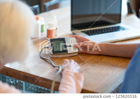 Female doctor helping senior patient with blood pressure test and pulse measurement 125620316