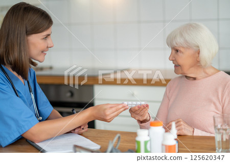 In-home nurse assisting senior patient with taking pills for disease treatment 125620347
