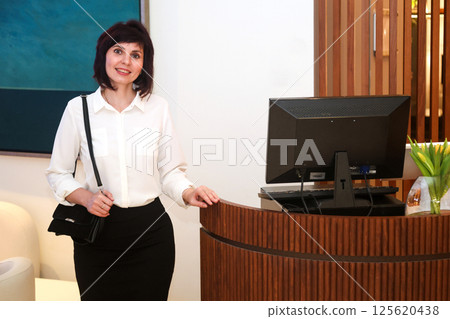 An office worker stands near her workstation with a computer on her desk 125620438