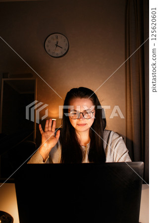 Young millennial woman starting video conference with greeting gesture. Smiling and friendly employee participating in remote video call. 125620601