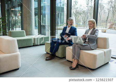 Professional colleagues using gadgets collaborating on couch negotiating partnership details Professional colleagues using gadgets collaborating on couch negotiating partnership details 125621507