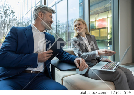 Businesspeople sitting on sofa discussing new project during conference briefing with computer Businesspeople sitting on sofa discussing new project during conference briefing with computer 125621509