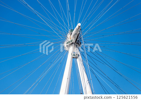 This detailed view showcases the intricate design of the London Eye's wheel and cables, highlighting its architectural beauty against a vibrant blue sky in London. 125621556