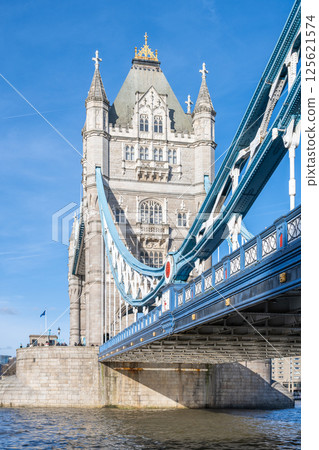 Tower Bridge stands majestically over the River Thames in London, showcasing its iconic architecture under a clear blue sky. The intricate design features both stone and metal elements. 125621574