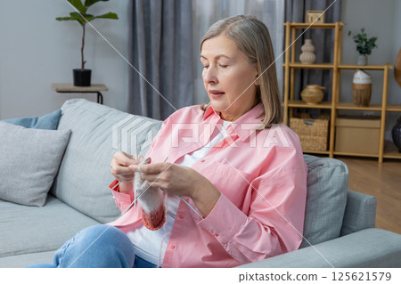 Woman in pink shirt sitting on the sofa and knitting Woman in pink shirt sitting on the sofa and knitting 125621579