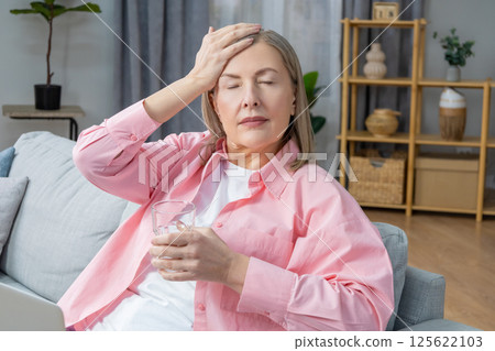 Woman sitting on the sofa and taking pills from a headache 125622103