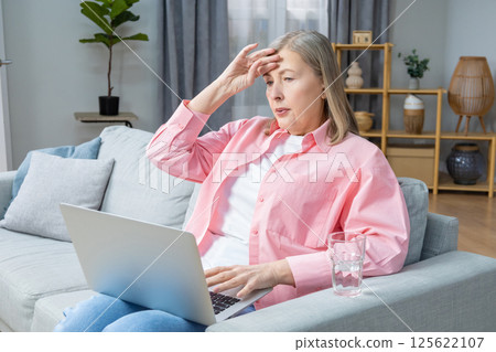 Mid aged woman in pink shirt feeling unwell and having a headache 125622107