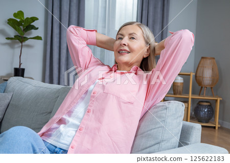 Smiling mid aged woman in pink shirt looking contented while spending time at home 125622183