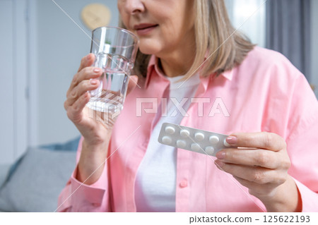 Mid aged woman in pink shirt taking HRT pills 125622193