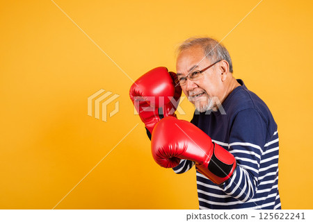 Portrait Asian old man wearing glasses wear two red boxing gloves studio shot isolated yellow background, smiling happy elderly man gray haired healthy fighter lifestyle concept Portrait Asian old man wearing glasses wear two red boxing gloves studio shot isolated yellow background, smiling happy elderly man gray haired healthy fighter lifestyle concept 125622241