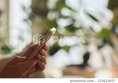A person is comfortably using their smartphone while sitting in a cozy, relaxed environment A person is comfortably using their smartphone while sitting in a cozy, relaxed environment 125622657