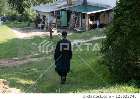 Male in black clothes walking on green grass to old house 125622745