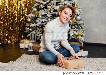 Woman smiling and decorating Christmas tree with new year gifts with toys 125622748