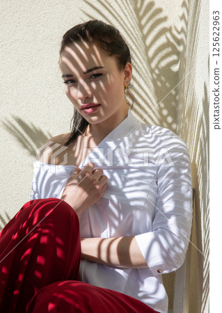 Beautiful brunette woman in summer sitting in the shade of a palm tree Beautiful brunette woman in summer sitting in the shade of a palm tree 125622963