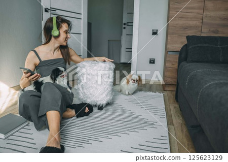 woman in casual wear with headphones interacting with her dogs in a modern living space, capturing a moment of joyful pet companionship woman in casual wear with headphones interacting with her dogs in a modern living space, capturing a moment of joyful pet companionship 125623129