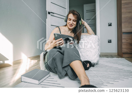 woman enjoying music and browsing on her phone with her dog by her side in a cozy, sunlit room woman enjoying music and browsing on her phone with her dog by her side in a cozy, sunlit room 125623130