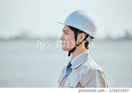 一位 20 多歲的年輕男子穿著工作服凝視遠方 一位 20 多歲的年輕男子穿著工作服凝視遠方 125623307