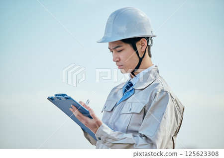 一名 20 多歲的年輕男子穿著工作服在做筆記 125623308
