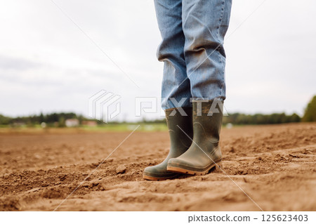 Close-up of a farmers legs in rubber boots walking through field. Concept of gardening, ecology. Close-up of a farmers legs in rubber boots walking through field. Concept of gardening, ecology. 125623403