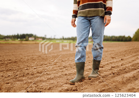 Close-up of a farmers legs in rubber boots walking through field. Concept of gardening, ecology. 125623404