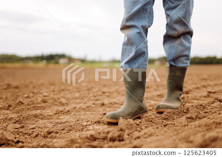 Close-up of a farmers legs in rubber boots walking through field. Concept of gardening, ecology. Close-up of a farmers legs in rubber boots walking through field. Concept of gardening, ecology. 125623405