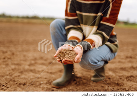 Young female farmer's hands touch dry soil in an agricultural field. Gardening and ecology concept. Young female farmer's hands touch dry soil in an agricultural field. Gardening and ecology concept. 125623406